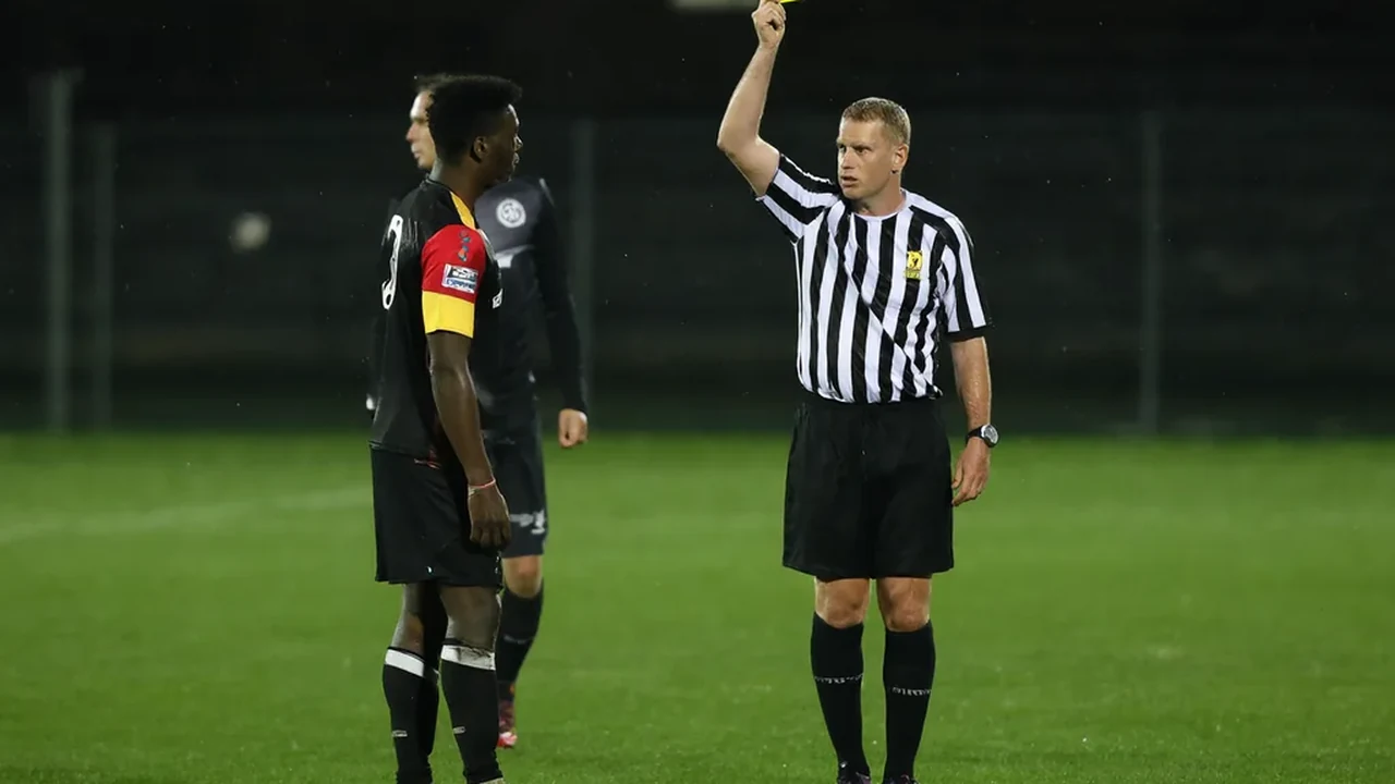 Referee holding a yellow card up to a player during a floodlit match