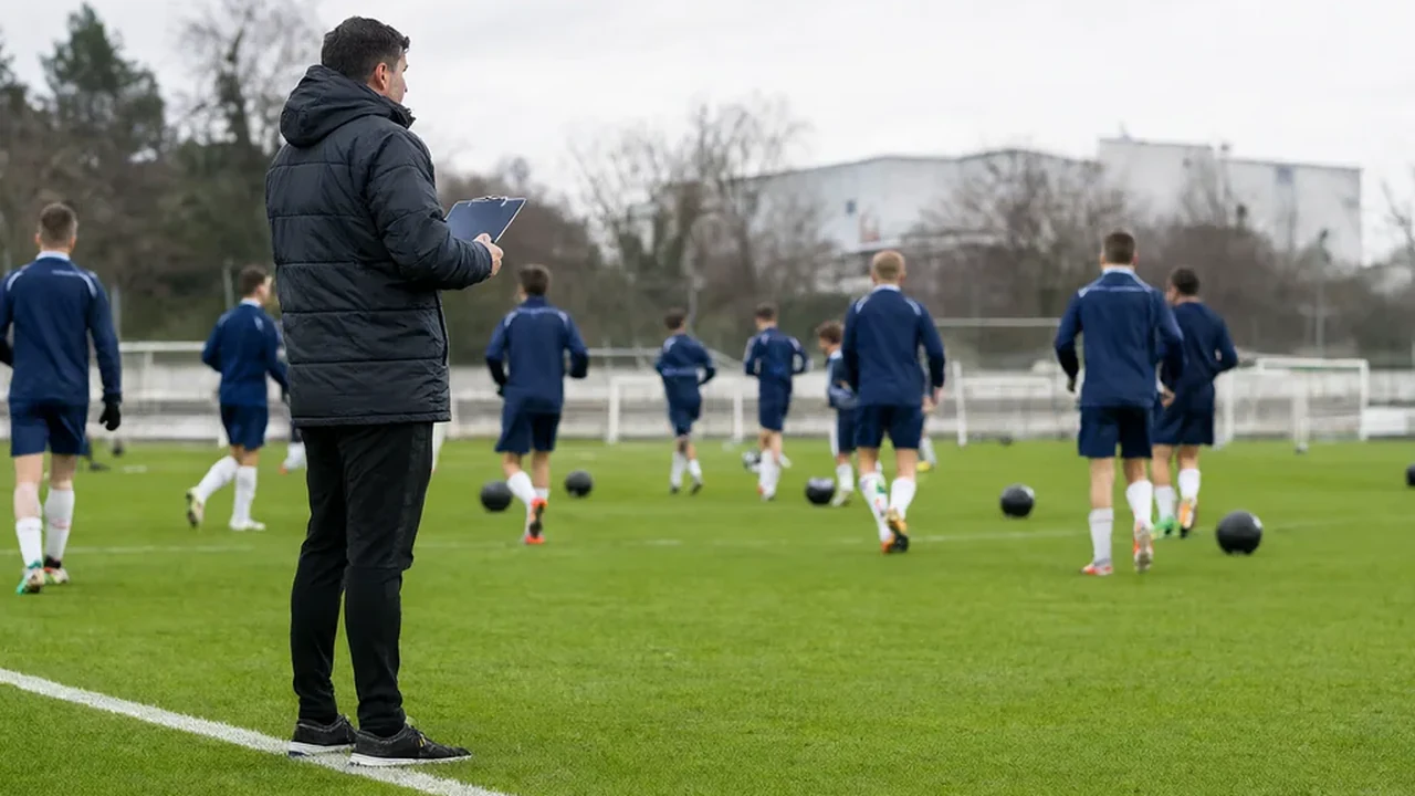 New head coach watching training from the side of the pitch with a clipboard